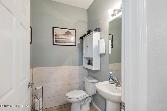 bathroom with a textured ceiling, sink, wood walls, tile patterned floors, and toilet