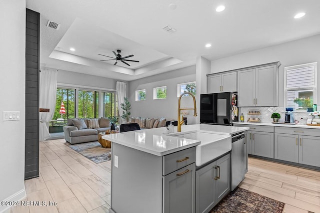 kitchen with sink, an island with sink, a raised ceiling, black fridge, and stainless steel dishwasher