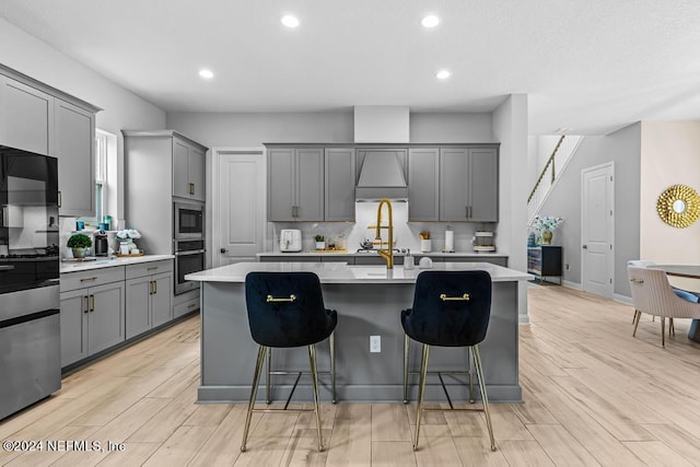 kitchen with an island with sink, light hardwood / wood-style flooring, gray cabinets, and stainless steel microwave