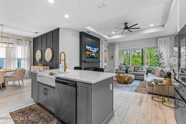 kitchen featuring a raised ceiling, ceiling fan with notable chandelier, dishwasher, light hardwood / wood-style floors, and gray cabinets