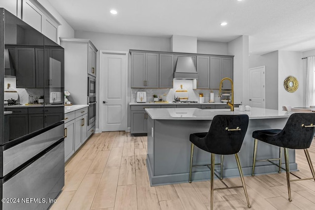 kitchen with gray cabinets, light wood-type flooring, and a center island with sink