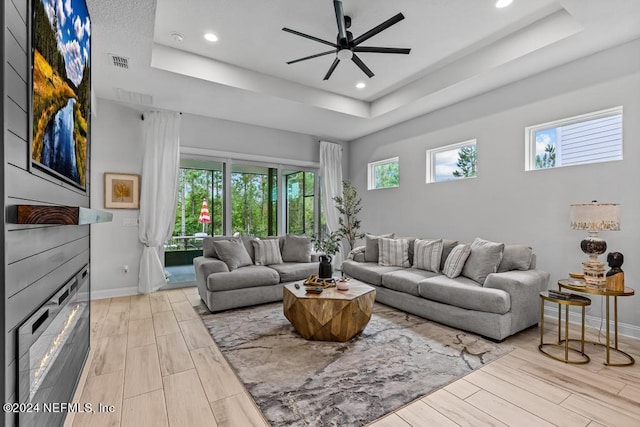 living room featuring light hardwood / wood-style floors, ceiling fan, and a raised ceiling