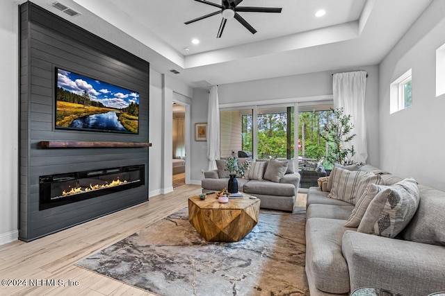 living room featuring a raised ceiling, ceiling fan, light wood-type flooring, and a fireplace