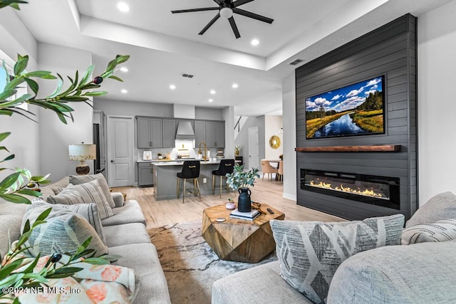 living room with ceiling fan, a fireplace, a raised ceiling, and light hardwood / wood-style flooring