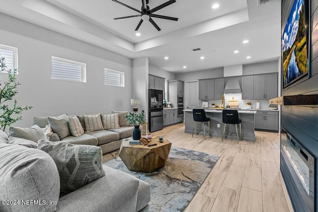 living room featuring a tray ceiling, light wood-type flooring, and ceiling fan