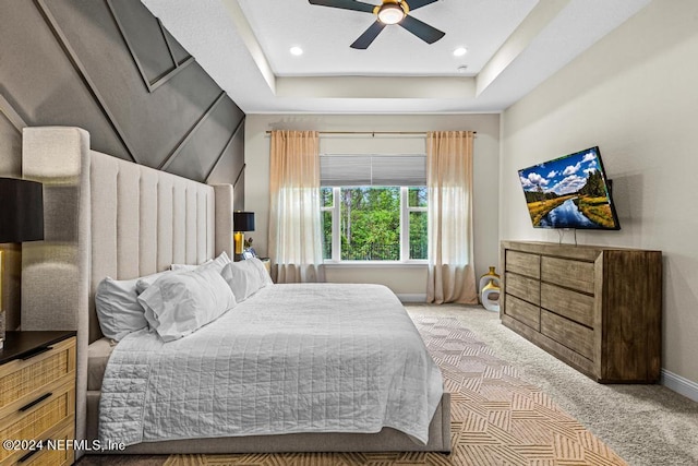 bedroom with ceiling fan, light carpet, and a tray ceiling