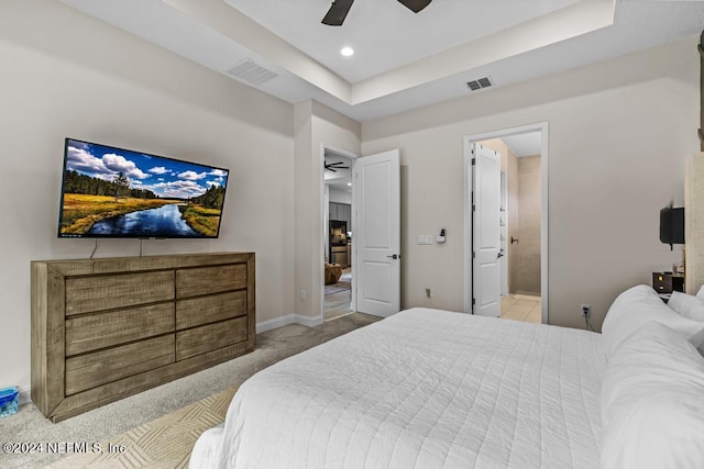 carpeted bedroom featuring a raised ceiling, connected bathroom, and ceiling fan