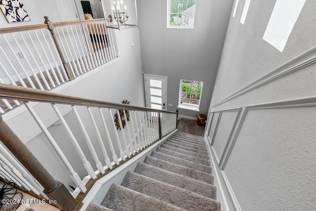 stairs featuring a towering ceiling, an inviting chandelier, and carpet