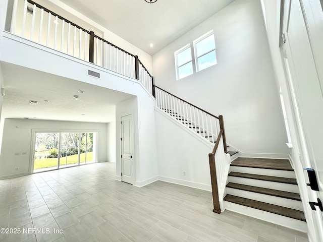 stairway with visible vents, baseboards, and a towering ceiling