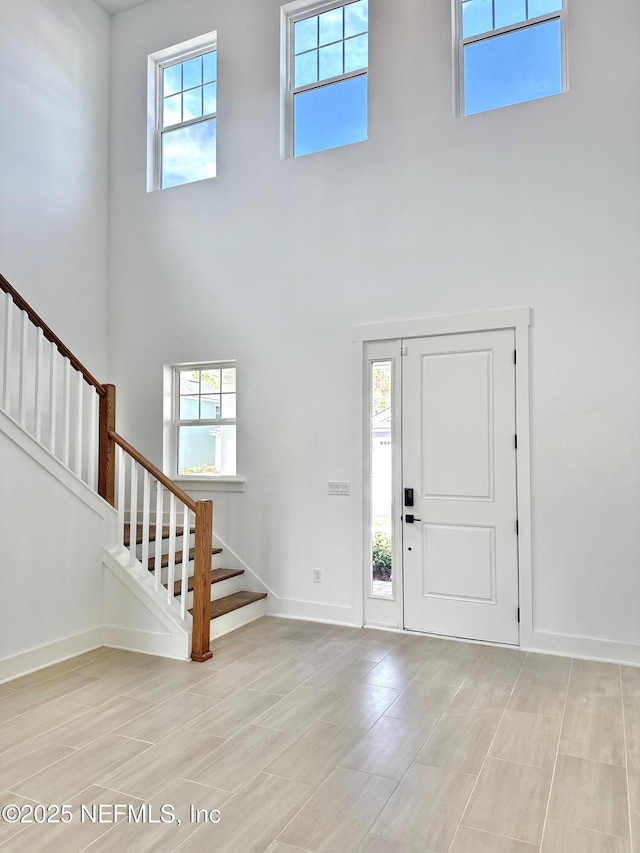 foyer featuring light wood-style flooring, a high ceiling, stairs, and baseboards