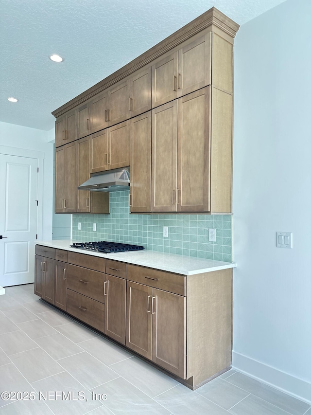 kitchen with under cabinet range hood, stainless steel gas stovetop, light countertops, light tile patterned floors, and decorative backsplash