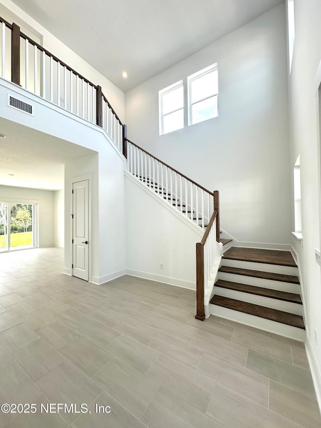 stairway featuring visible vents, baseboards, and a towering ceiling