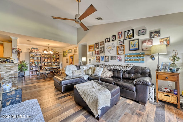 living room featuring ceiling fan with notable chandelier, ornamental molding, wood-type flooring, and lofted ceiling