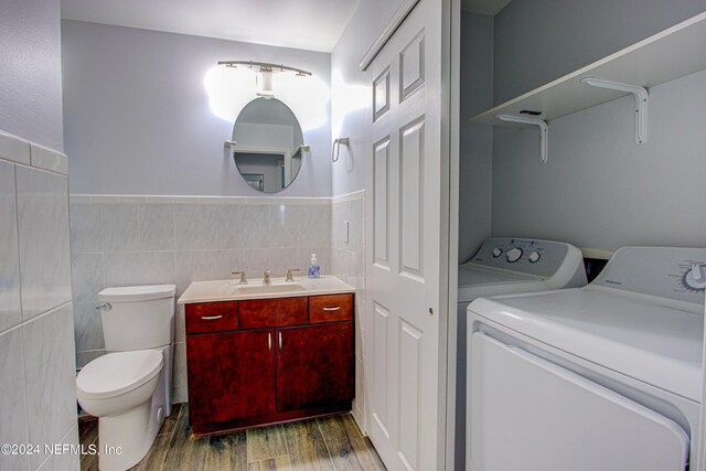 laundry area with dark wood-type flooring, tile walls, washing machine and clothes dryer, and sink