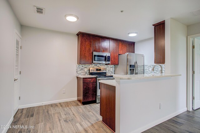 kitchen featuring appliances with stainless steel finishes, light hardwood / wood-style floors, sink, kitchen peninsula, and tasteful backsplash