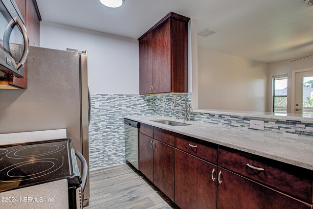 kitchen with light stone countertops, light hardwood / wood-style flooring, appliances with stainless steel finishes, tasteful backsplash, and sink