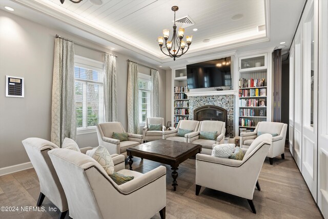 living room with built in shelves, a raised ceiling, a chandelier, a fireplace, and light wood-type flooring