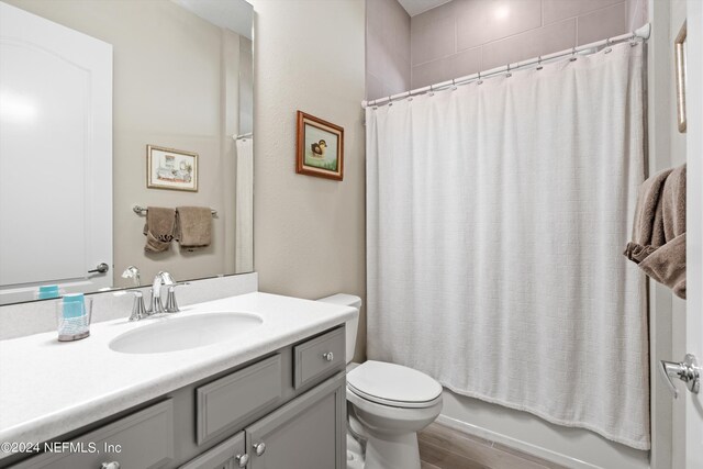 full bathroom featuring hardwood / wood-style floors, vanity, shower / tub combo, and toilet