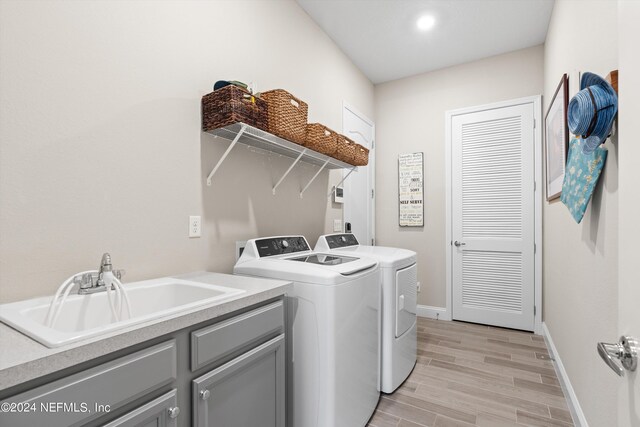 washroom featuring cabinets, sink, washer and dryer, and light hardwood / wood-style flooring