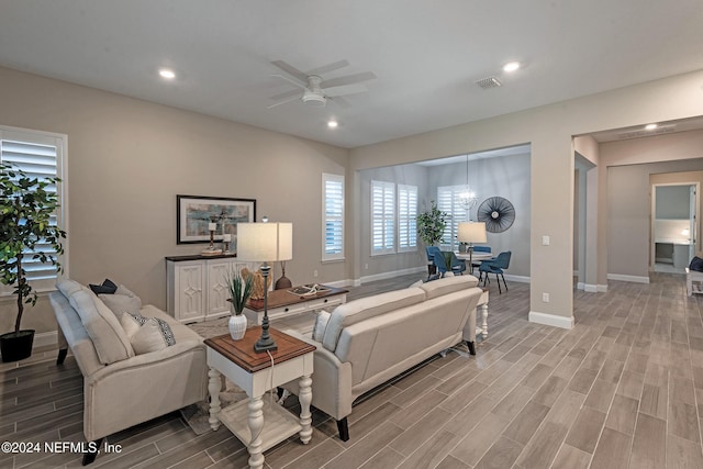 living room with ceiling fan with notable chandelier and light hardwood / wood-style floors