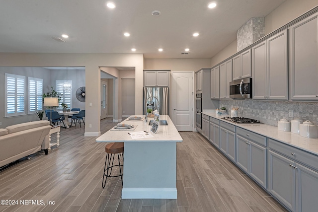 kitchen with gray cabinets, an island with sink, stainless steel appliances, and light hardwood / wood-style floors