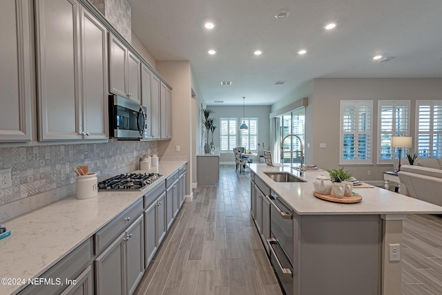 kitchen featuring light stone countertops, sink, stainless steel appliances, light hardwood / wood-style floors, and a center island with sink