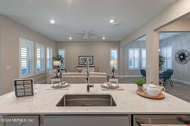 kitchen with light stone countertops, hardwood / wood-style flooring, a wealth of natural light, and a kitchen island with sink