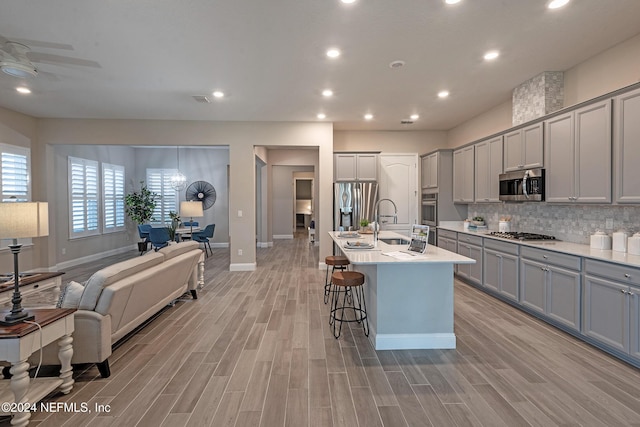 kitchen with a center island with sink, light hardwood / wood-style floors, gray cabinetry, and stainless steel appliances