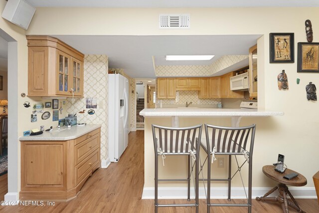 kitchen featuring backsplash, kitchen peninsula, light wood-type flooring, and white appliances