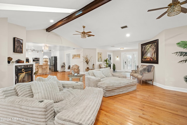 living room with lofted ceiling with beams, light hardwood / wood-style flooring, a high end fireplace, and ceiling fan