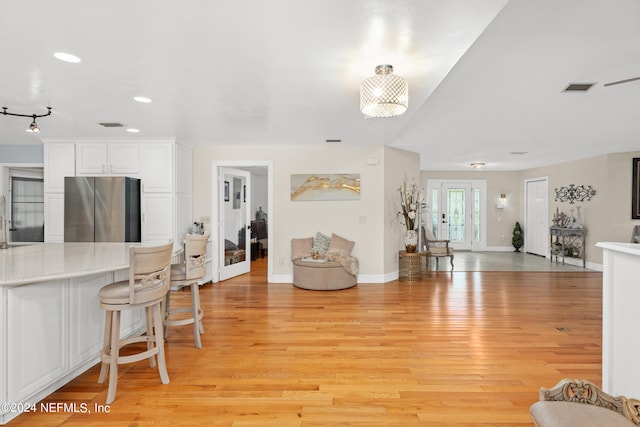 interior space featuring a kitchen breakfast bar, white cabinetry, light hardwood / wood-style flooring, and stainless steel refrigerator