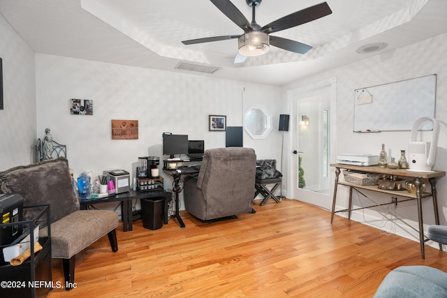 office space featuring ceiling fan, a tray ceiling, and light wood-type flooring