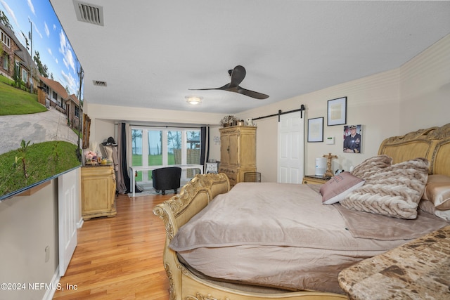 bedroom featuring ceiling fan, a barn door, light hardwood / wood-style flooring, and a textured ceiling