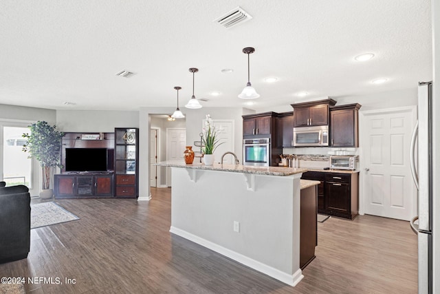 kitchen with wood-type flooring, a kitchen breakfast bar, stainless steel appliances, a center island with sink, and decorative light fixtures