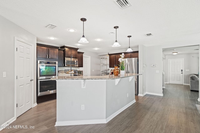 kitchen featuring light stone counters, a breakfast bar, dark hardwood / wood-style flooring, stainless steel appliances, and a center island with sink