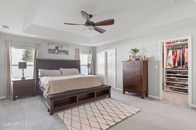 bedroom featuring ceiling fan, a raised ceiling, a walk in closet, a closet, and light carpet