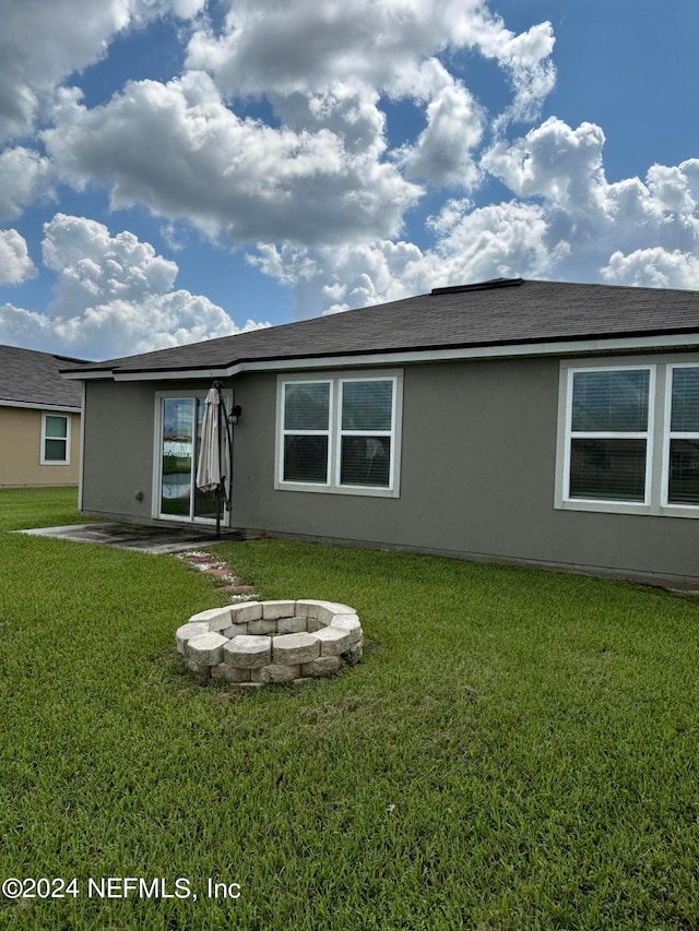 rear view of house featuring a patio, a yard, and an outdoor fire pit