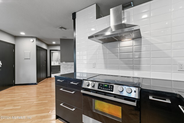 kitchen with wall chimney range hood, stainless steel electric range oven, decorative backsplash, and light hardwood / wood-style flooring