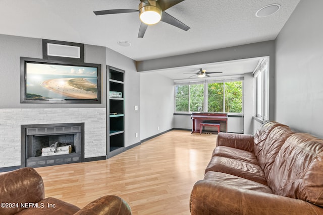 living room with hardwood / wood-style flooring, built in shelves, a stone fireplace, ceiling fan, and a textured ceiling