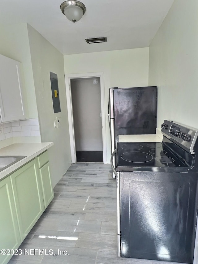 interior space featuring backsplash, green cabinets, electric panel, black electric range oven, and light wood-type flooring