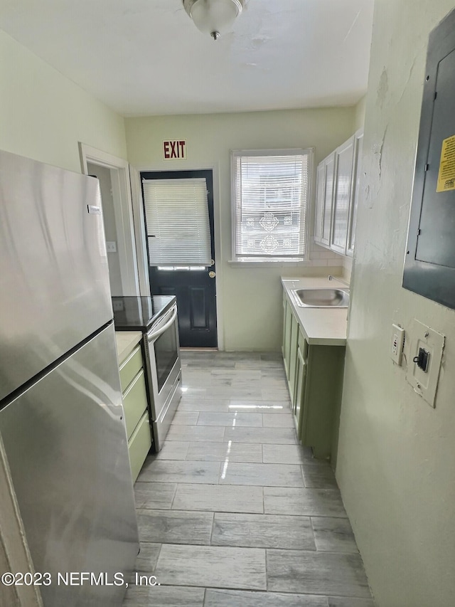 kitchen featuring light hardwood / wood-style flooring, green cabinetry, stainless steel appliances, electric panel, and sink