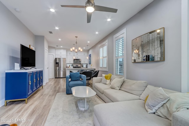 living room with ceiling fan with notable chandelier and light wood-type flooring