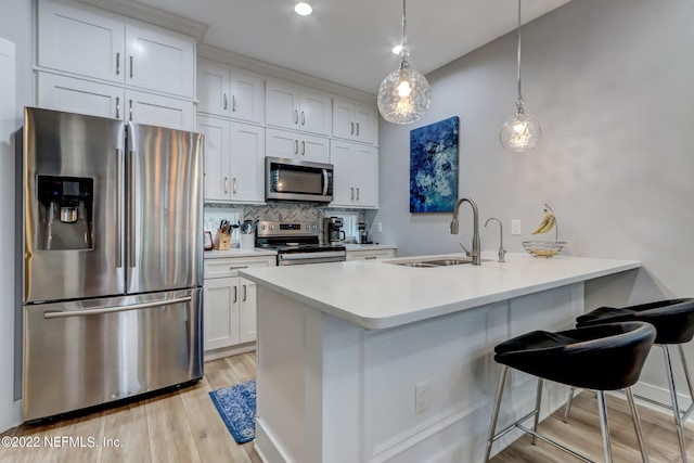 kitchen featuring stainless steel appliances, sink, a breakfast bar, decorative light fixtures, and white cabinets