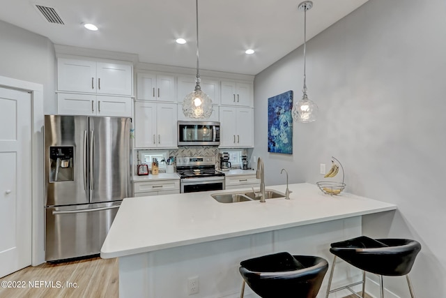 kitchen with hanging light fixtures, backsplash, sink, white cabinets, and appliances with stainless steel finishes