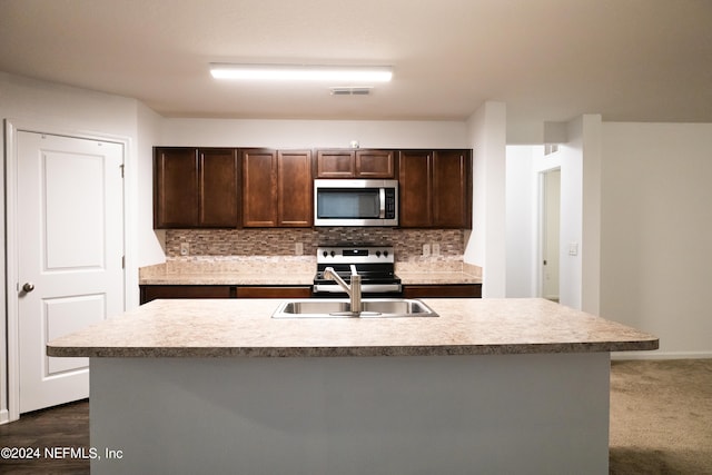 kitchen featuring decorative backsplash, dark brown cabinetry, sink, stainless steel appliances, and an island with sink