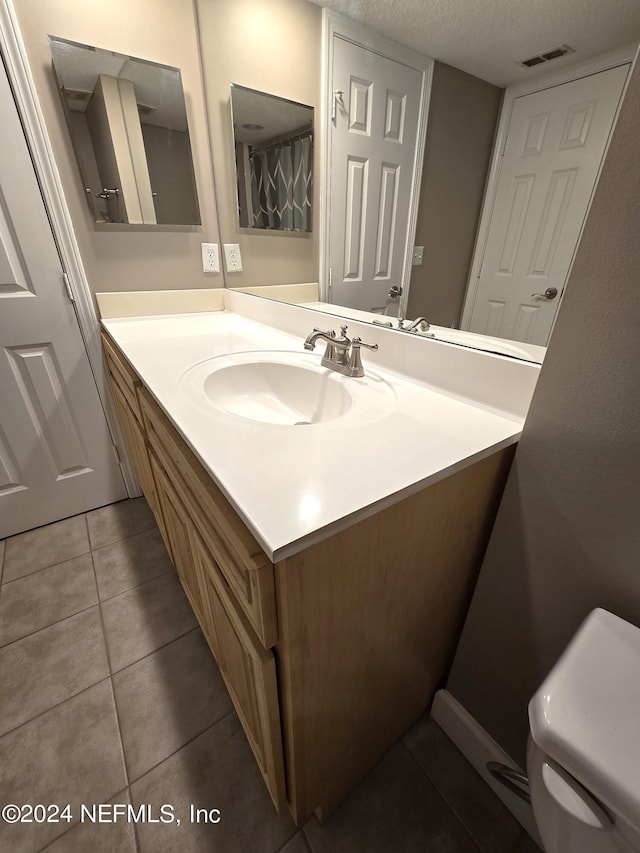 bathroom featuring tile patterned flooring, vanity, toilet, and a textured ceiling