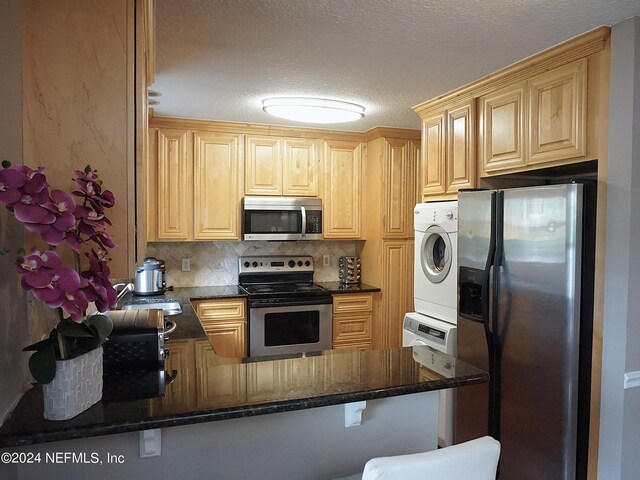 kitchen featuring a textured ceiling, backsplash, stacked washer and dryer, stainless steel appliances, and kitchen peninsula