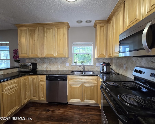 kitchen featuring a textured ceiling, dark hardwood / wood-style floors, appliances with stainless steel finishes, sink, and dark stone counters