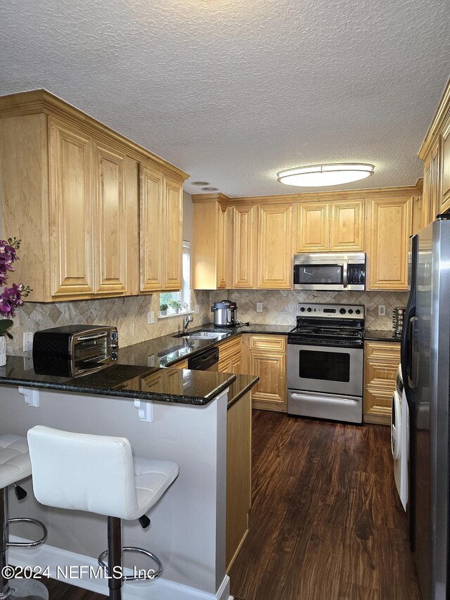 kitchen featuring appliances with stainless steel finishes, kitchen peninsula, dark wood-type flooring, a kitchen breakfast bar, and a textured ceiling