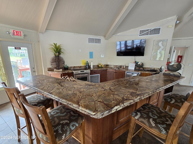 kitchen featuring kitchen peninsula, sink, vaulted ceiling with beams, appliances with stainless steel finishes, and a breakfast bar area